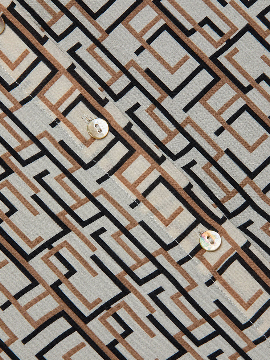 Close-up of the L'Agence Nina Silk Blouse in Ecru Multi Geo Print featuring black and brown geometric patterns and visible buttons, set against a light beige background.