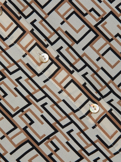 Close-up of the L'Agence Nina Silk Blouse in Ecru Multi Geo Print featuring black and brown geometric patterns and visible buttons, set against a light beige background.