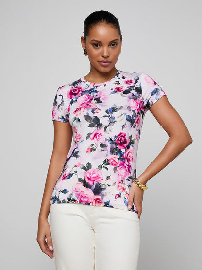 A woman poses against a plain light background wearing the L'Agence Ressi Fitted Tee in Pink Multi Water Rose, paired with white pants.