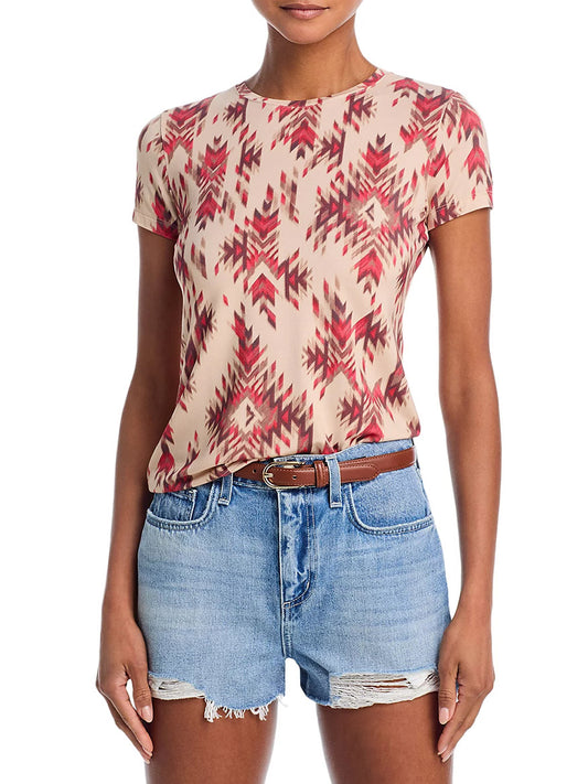 A woman wears the L'Agence Ressi Fitted Tee in Tan Multi Ganado Print, paired with blue denim cut-off shorts and a brown belt, standing against a plain background.