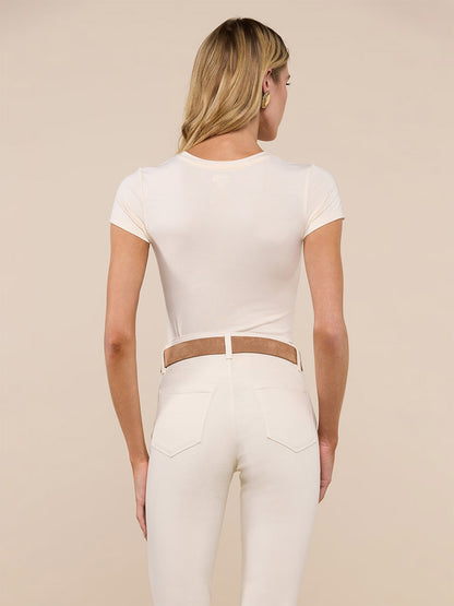A woman stands with her back to the camera, wearing the bestselling L'Agence Ressi Fitted Tee in Vintage White and high-waisted cream pants featuring brown belt detailing.