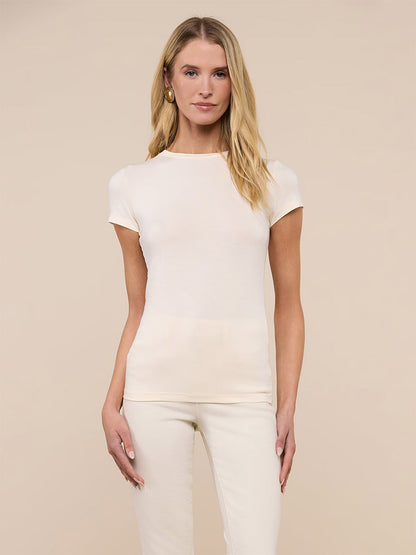 Woman wearing the L'Agence Ressi Fitted Tee in Vintage White, styled with matching pants, standing against a plain beige background.