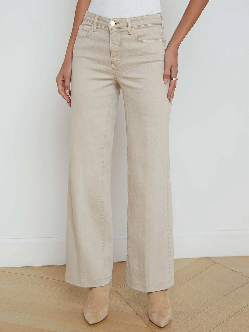 Someone wears the L'Agence Scottie Wide-Leg Jean in Biscuit with beige pointed-toe shoes, standing against a white wall on a wooden floor.