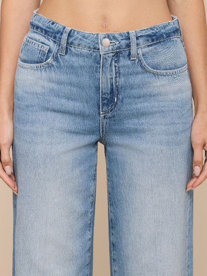 Close-up of a person wearing the L'Agence Scottie Wide-Leg Jean in Grant, a high-rise, light blue all-cotton denim style with button and zipper front, standing against a neutral background.