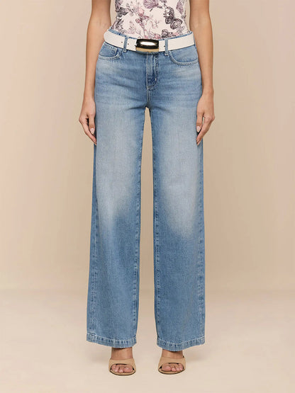 Someone stands against a plain beige background wearing L'Agence Scottie Wide-Leg Jean in Grant, a white belt, a floral top, and beige open-toe heels.