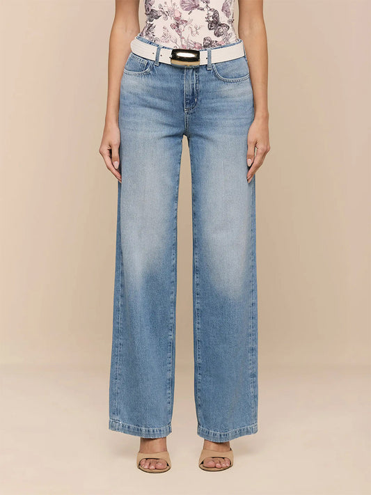 Someone stands against a plain beige background wearing L'Agence Scottie Wide-Leg Jean in Grant, a white belt, a floral top, and beige open-toe heels.