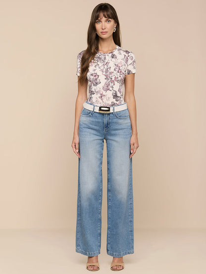 A woman stands against a plain background wearing a floral print t-shirt, the L'Agence Scottie Wide-Leg Jean in Grant, a white belt, and heeled sandals.