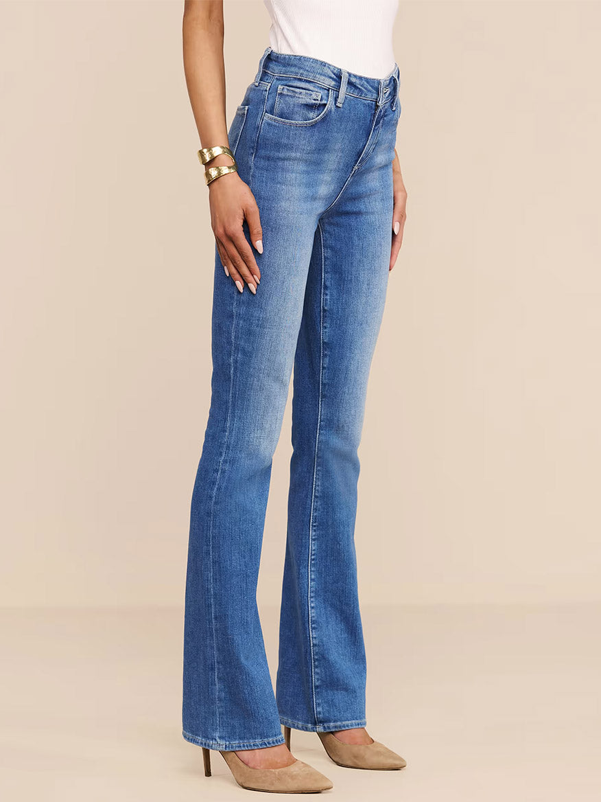 A woman models the L'Agence Selma Bootcut Jean in Sullivan with a white top and tan high heels against a neutral background.