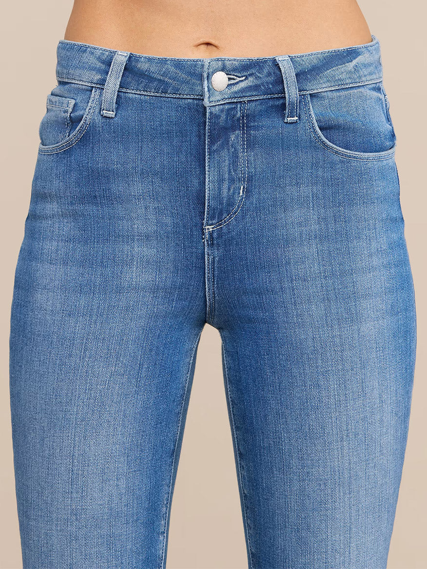 Close-up of a person wearing the L'Agence Selma Bootcut Jean in Sullivan—high-waisted, light blue stretch denim jeans with a button and zipper closure, front pockets, and belt loops. Only the waist and upper legs are visible.