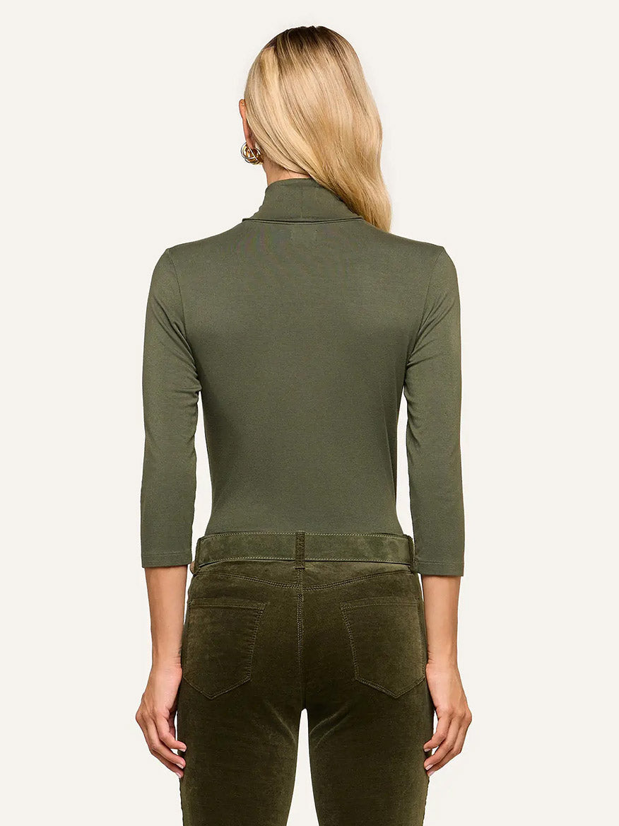 A person stands with their back to the camera, wearing the L’Agence Aja Turtleneck in Army and matching ultra-soft knit pants.
