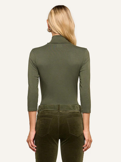 A person stands with their back to the camera, wearing the L’Agence Aja Turtleneck in Army and matching ultra-soft knit pants.