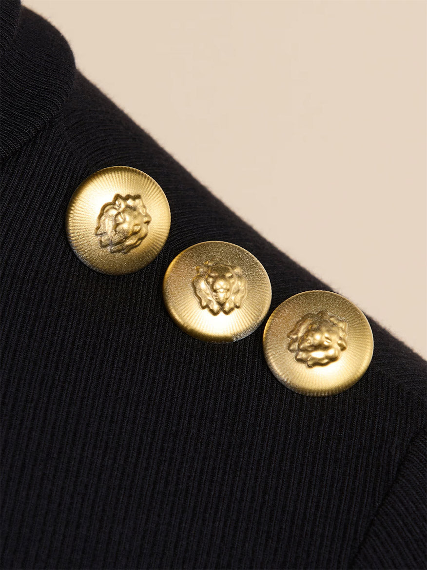 Close-up of three gold, lion-embossed buttons on the L’Agence Aja Turtleneck in Black/Gold, crafted from luxe ribbed modal.