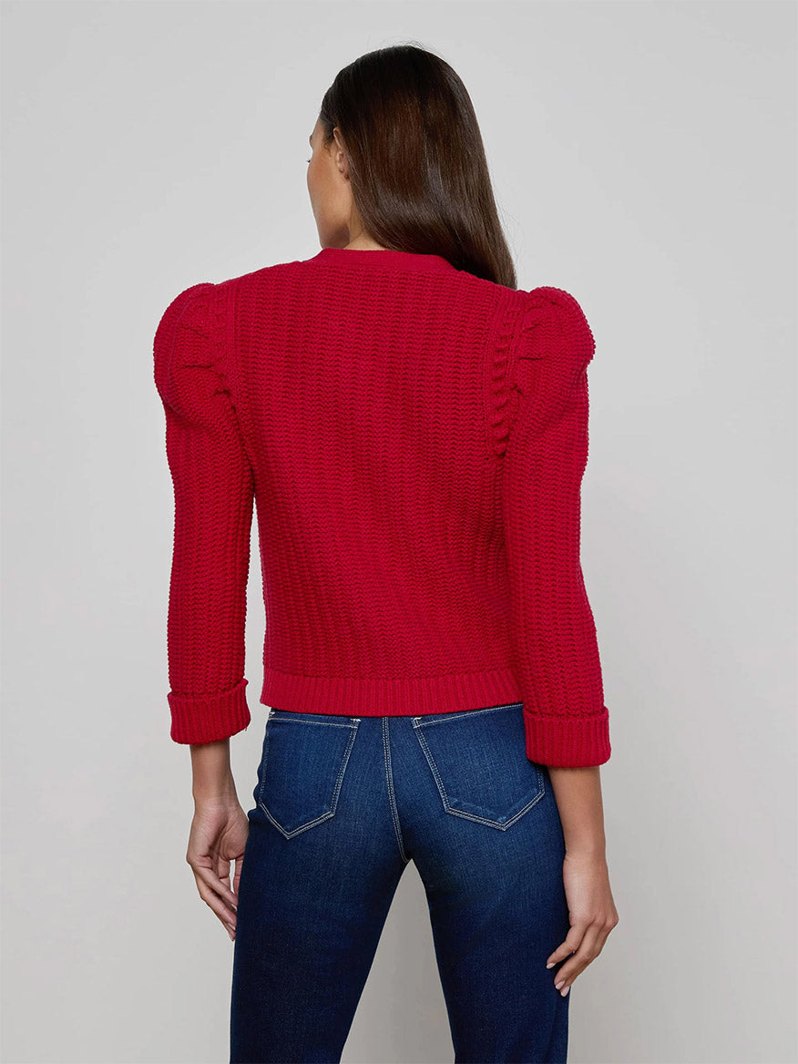 A woman is seen from behind wearing the L'Agence Delli Cropped Cardigan in Engine Red/Gold with blue jeans, set against a plain background.