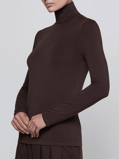 Wearing the L’Agence Lani Turtleneck in Dark Java, this person stands against a plain light background, shown from shoulders to hips.