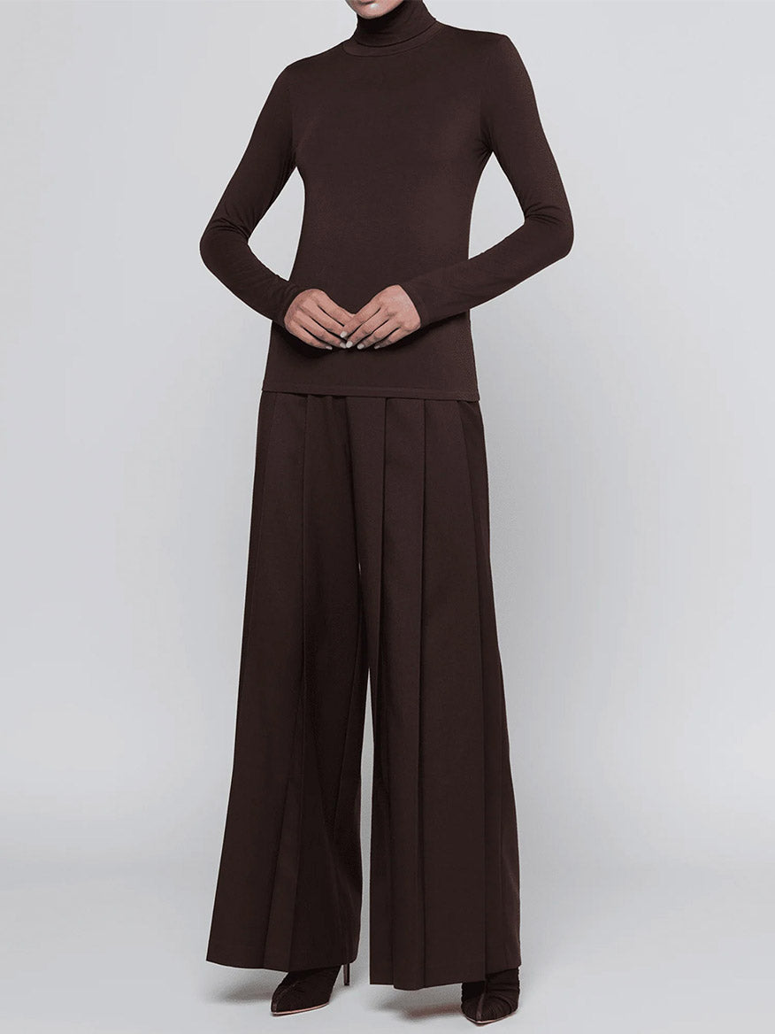 A person wearing the L’Agence Lani Turtleneck in Dark Java and wide-legged pleated brown pants, standing against a plain light background.