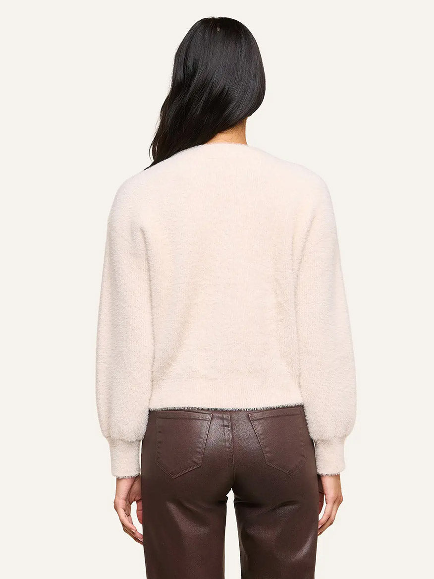 A person with long dark hair shown from the back, wearing the L’Agence Nimbus Pullover in Vintage White and high-waisted brown leather pants, set against a plain background.