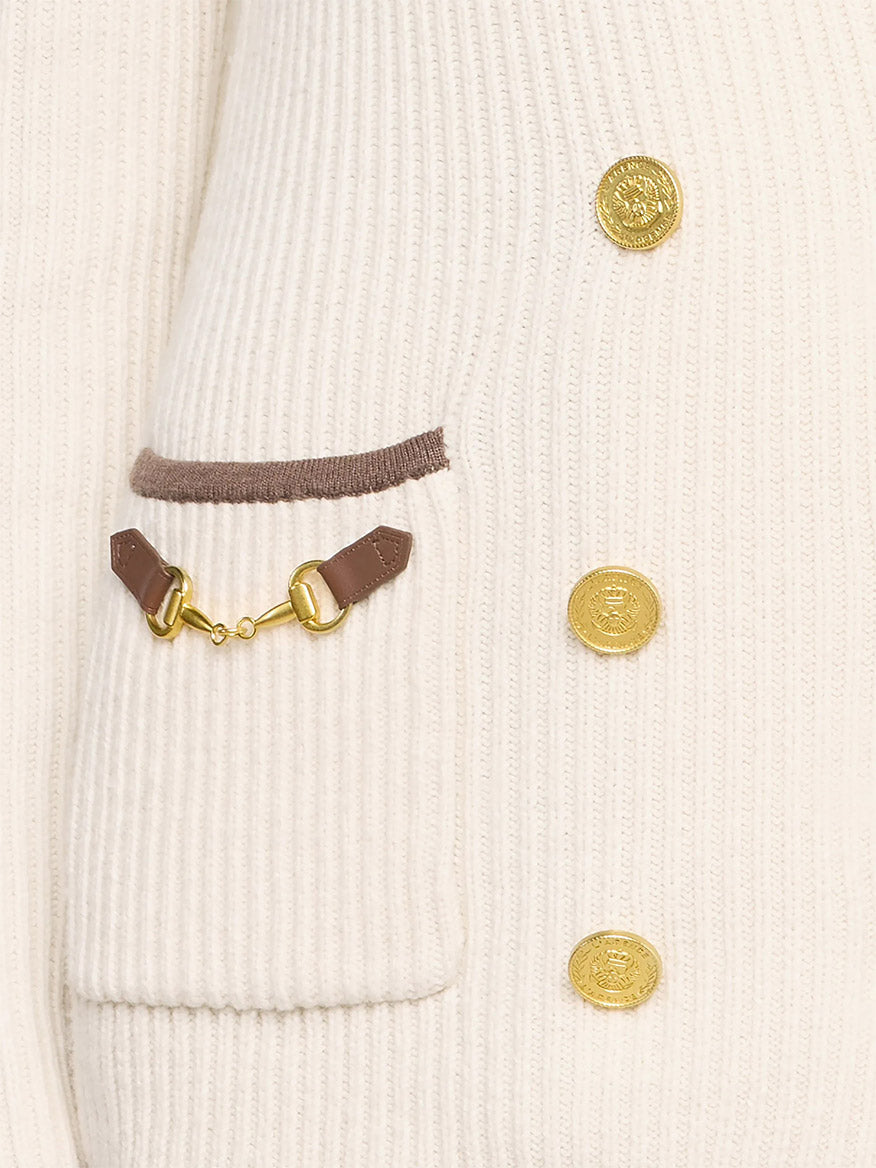 Close-up of the L’Agence Ranch Knit Blazer in Ivory/Dark Cappuccino, featuring a cream ribbed knit design, gold buttons, a pocket with dark cappuccino trim, and a decorative brown leather strap with a gold clasp.