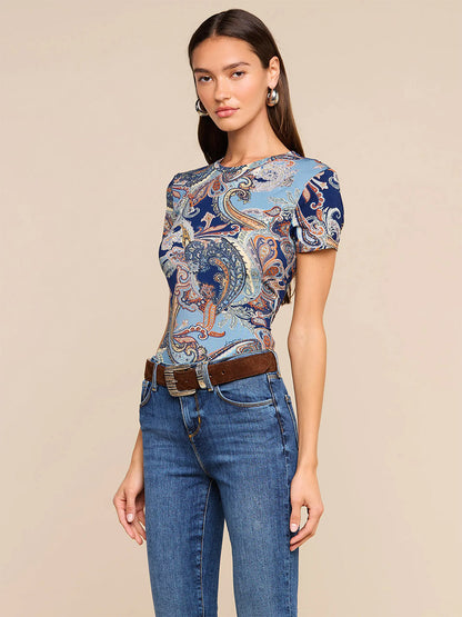 Woman wearing the L’Agence Ressi Fitted Tee in Midnight Multi Besarabian Paisley, paired with blue jeans and a brown belt, standing against a plain beige background. This stylish look is thoughtfully made in Los Angeles.