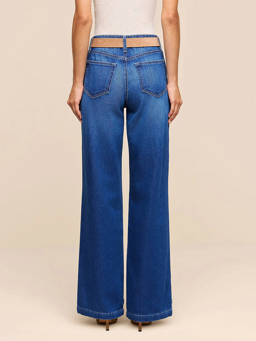 A person is seen from the back against a plain background, wearing the L’Agence Scottie Wide-Leg Jean in Idaho—high-waisted, wide-leg blue jeans made from nonstretch denim and featuring a distinctive cutout waistband.