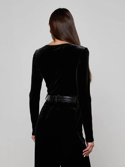A person with long brown hair faces away, wearing the L'Agence Seraphine Velvet Bodysuit in Black with long sleeves and matching belted pants against a plain light background. This stylish look is made in Los Angeles.