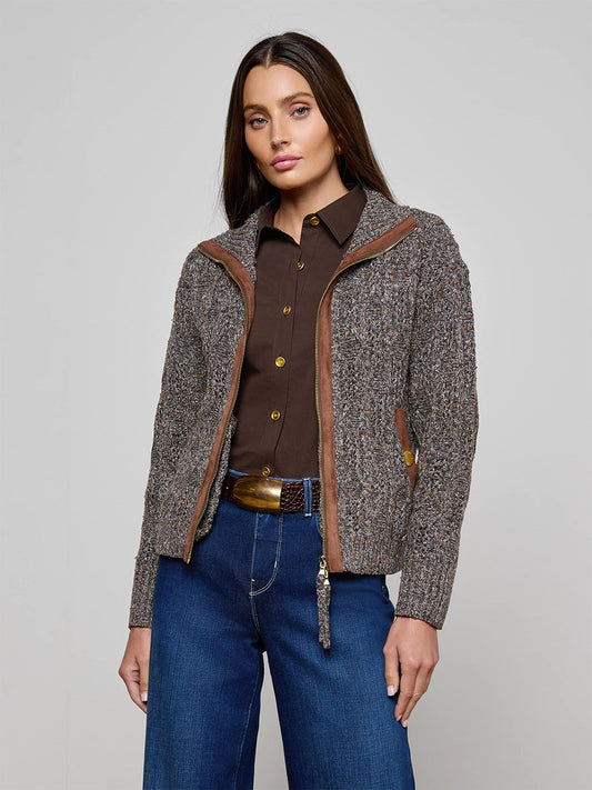 Woman standing against a plain background, wearing the L'Agence Shiloh Cable Knit Cardigan in Carafe Brown Multi, paired with blue jeans and a brown belt.