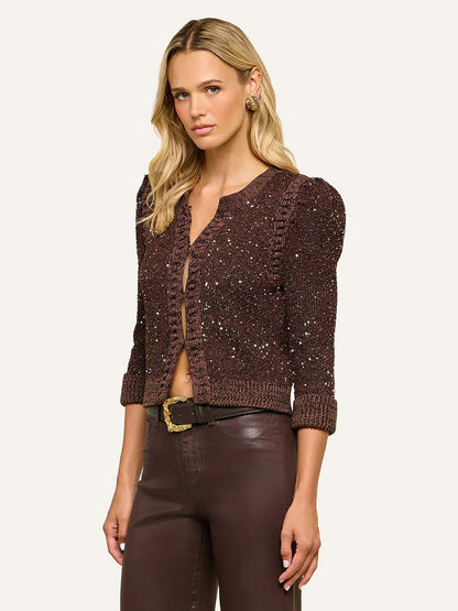 A woman wearing the L’Agence Thistle Sequined Cardigan in Black/Java/Sequins with micro sequin detailing and puffed shoulders, styled with brown high-waisted pants and standing against a plain background—the perfect look for Fall 2026.