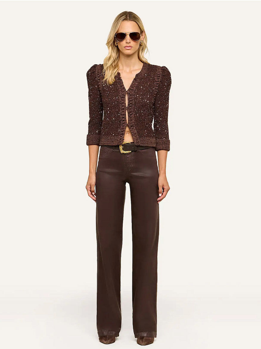 Woman wearing sunglasses, the L’Agence Thistle Sequined Cardigan in Black/Java/Sequins with puffed shoulders and subtle micro sequins, paired with brown high-waisted wide-leg pants and brown shoes, standing against a plain background—an effortlessly chic look for Fall 2026.
