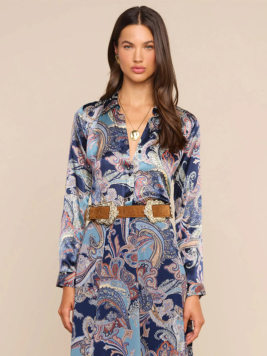 Woman wearing the L’Agence Tyler Blouse in Midnight Multi Besarabian Paisley, featuring long sleeves and a paisley print in blue and purple hues, styled with a gold necklace and a wide brown belt with large gold buckles.