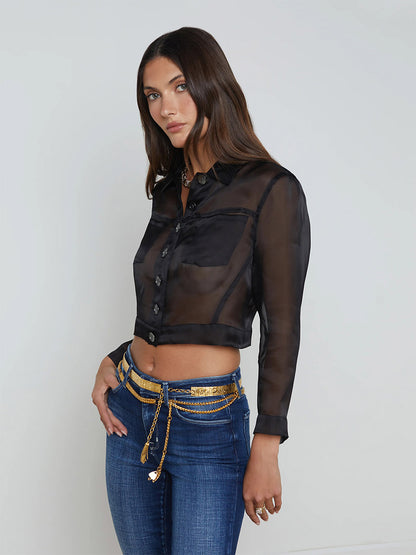 Woman wearing the L'Agence Anders Silk Organza Jacket in Black, paired with blue jeans and a gold chain belt, stands against a plain background.