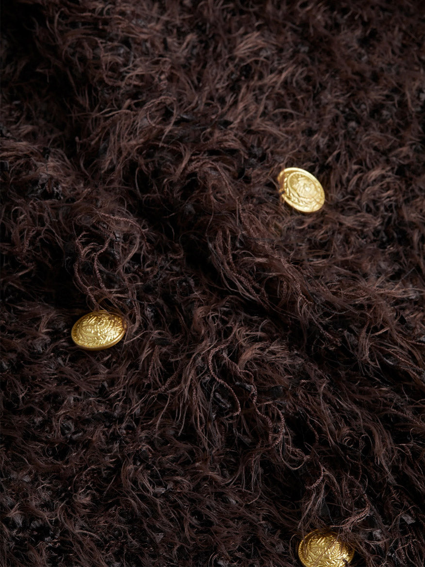 Close-up of a fluffy brown textured fabric adorned with decorative embossed dome buttons, capturing the elegance reminiscent of the L'Agence Azure Cardigan Blazer in Chocolate Ganache.