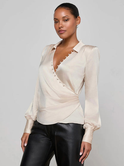 A woman showcases romantic elegance in the L'Agence Bernice Satin Wrap Blouse in Champagne and black leather pants, standing against a plain light gray background.
