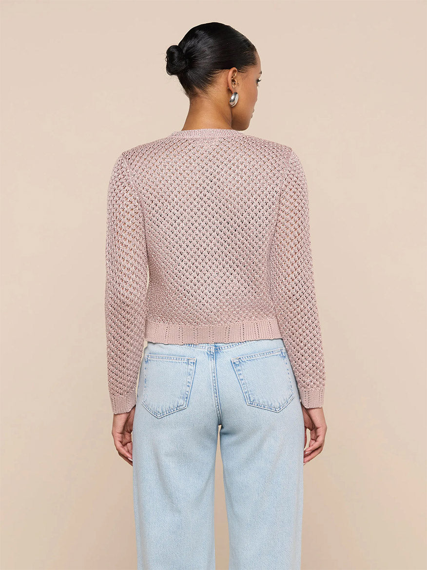 Woman stands with her back to the camera in the L'Agence Blanca Sequin Cardigan in Adobe Rose and light blue high-waisted jeans, set against a plain beige background.