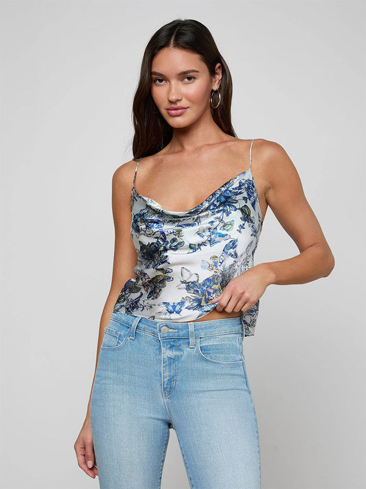 A woman wearing the L'Agence Calista Silk Camisole in Grey Multi Watercolor Butterfly and light blue jeans stands against a plain light gray background.