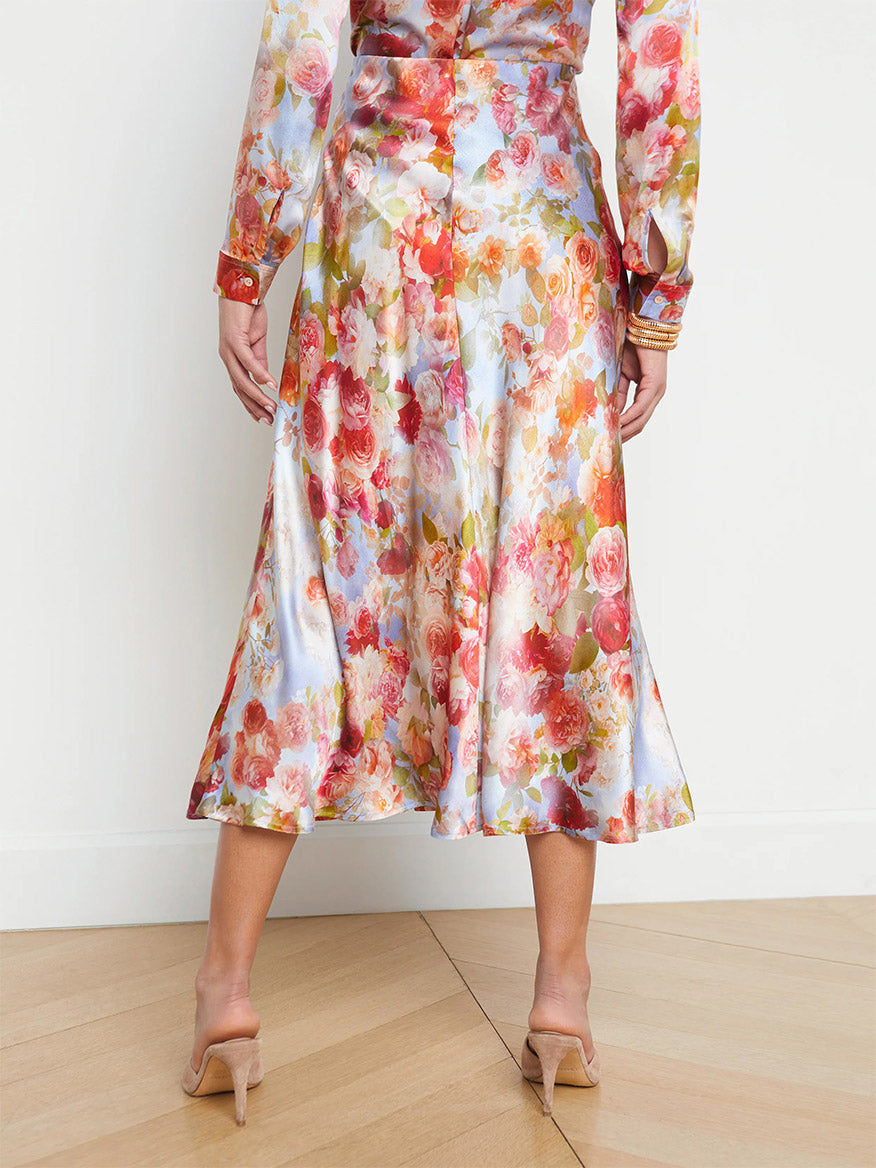 A person wearing a L'Agence Clarisa Silk Skirt in Multi Soft Cloud Floral and beige high heels, standing in front of a plain wall, focused on the lower half of their body.