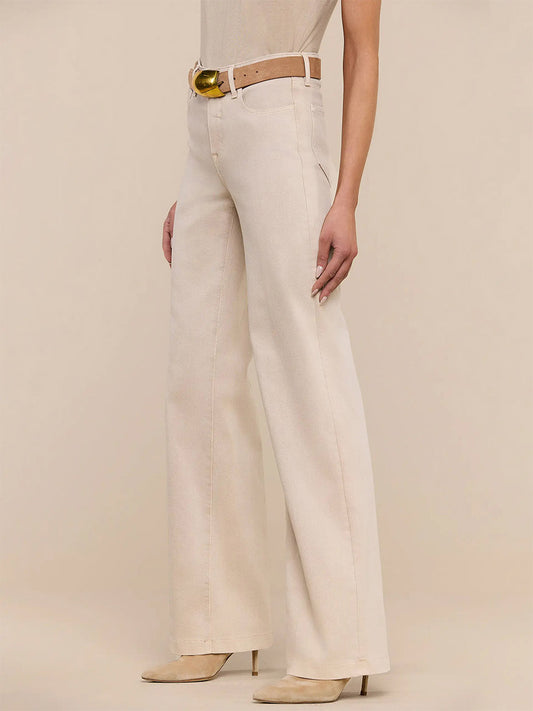 A person stands in a neutral pose wearing L'Agence Clayton Wide-Leg Jean in Biscuit, styled with a tan belt featuring a gold buckle, a beige top, and matching beige heeled boots against a plain background.