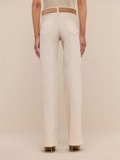 A person stands facing away from the camera, wearing L'Agence Clayton Wide-Leg Jean in Biscuit paired with a brown belt and beige high-heeled shoes against a plain background.