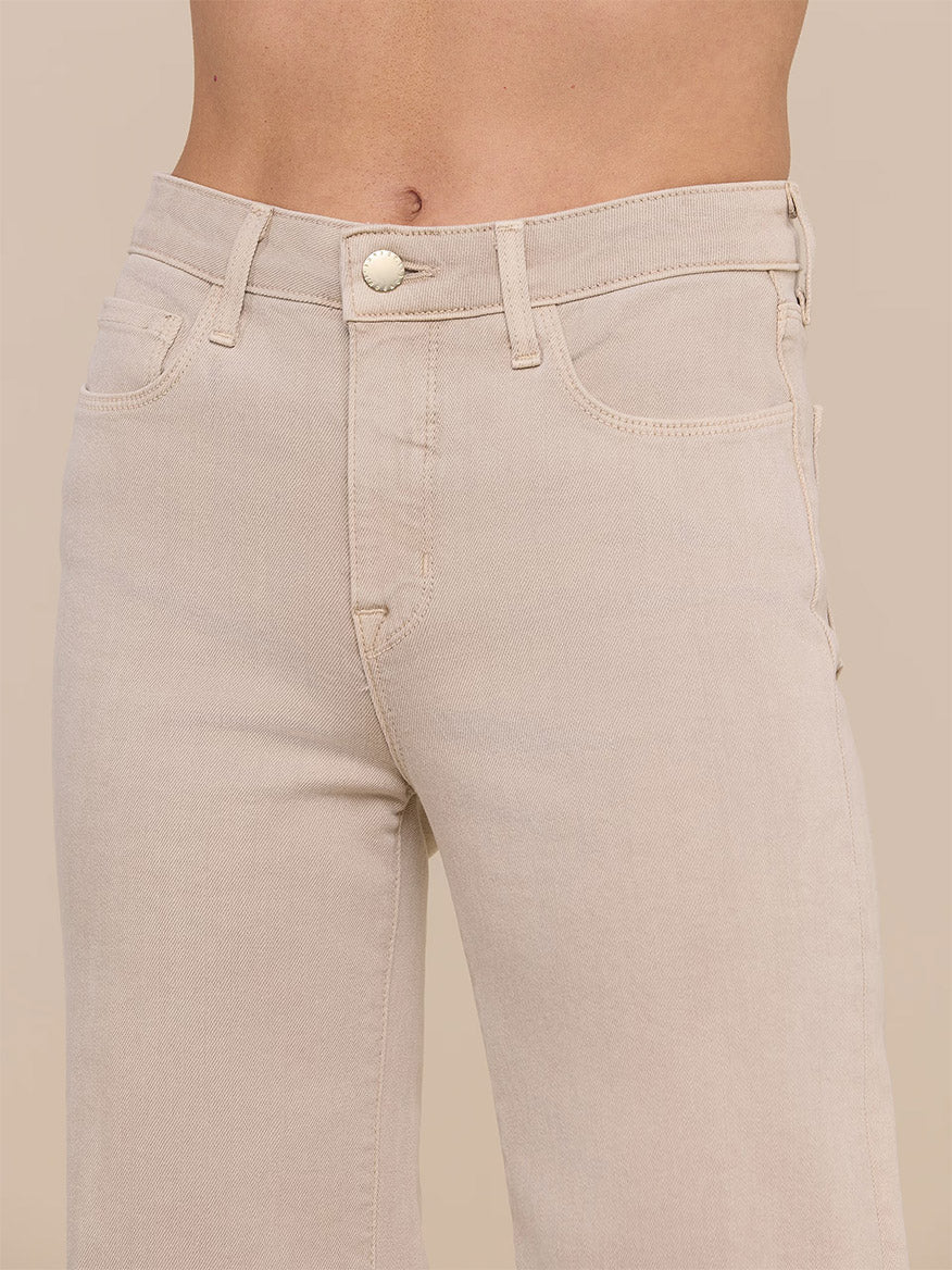 Close-up of a person wearing the L'Agence Clayton Wide-Leg Jean in Biscuit, a high-rise, light beige stretch denim with button closure and front pockets, shown from waist to mid-thigh.