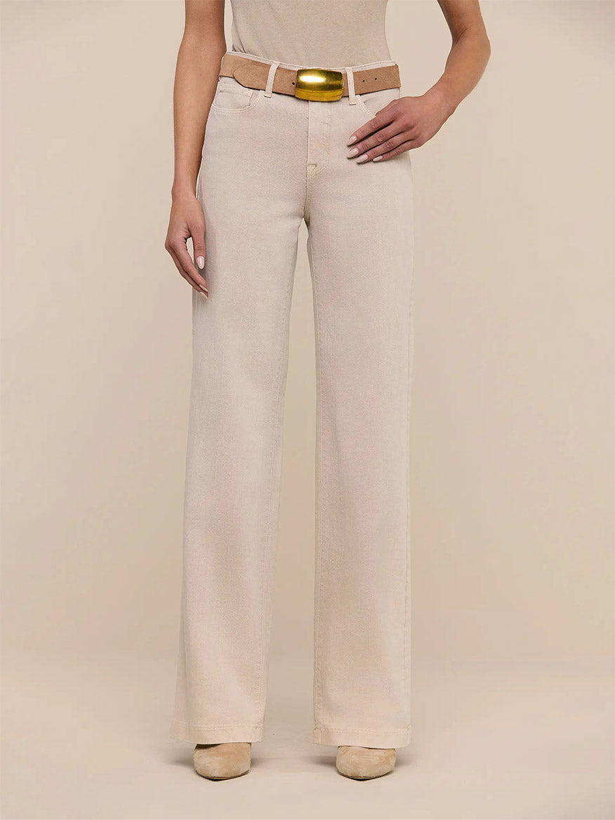 Someone wears the L'Agence Clayton Wide-Leg Jean in Biscuit, styled with a tan belt and beige shoes, posing against a neutral background.