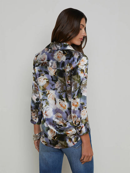 A woman with long hair is wearing a L'Agence Dani Blouse in Multi Distressed Floral and blue jeans, facing slightly away.