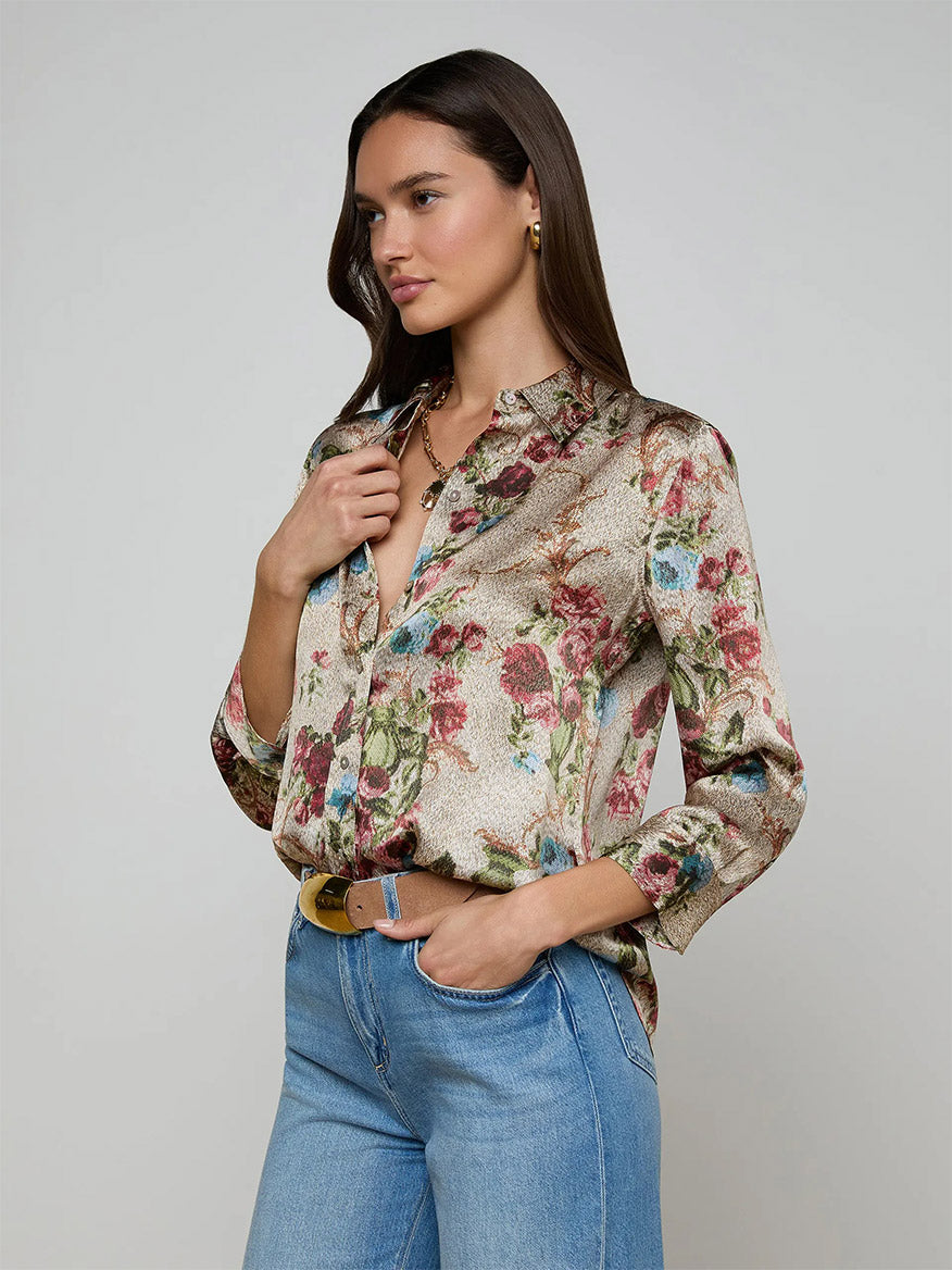 A woman models the L'Agence Dani Blouse in Multi Floral Tapestry with rolled sleeves, styled with light blue jeans against a plain background.