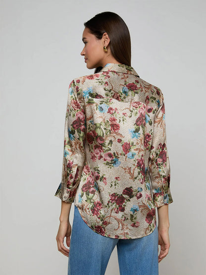 A woman faces away, wearing the L'Agence Dani Blouse in Multi Floral Tapestry with blue jeans against a plain light background.