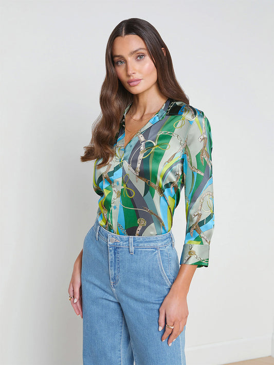 Woman in a colorful printed L'Agence Dani Blouse in Sea Green Multi Belt and blue jeans standing against a plain white background.