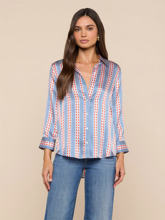 A woman wears the L'Agence Dani Blouse in Blue/Red Textured Stripe Print— a long-sleeve silk button-down with blue, white, and red stripes—paired with blue jeans against a plain beige background.