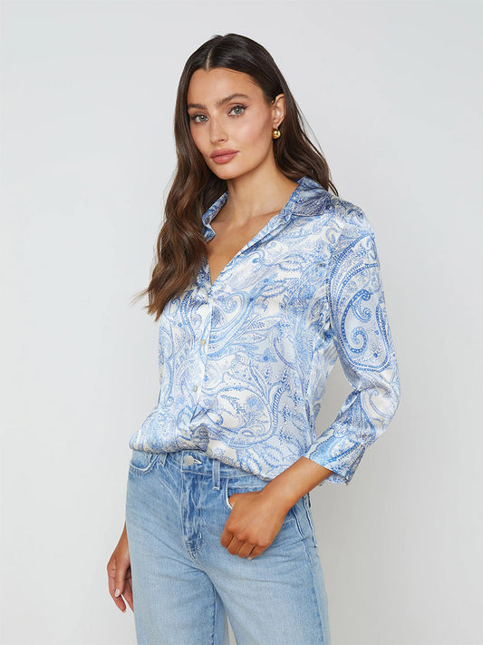 A woman models a L'Agence Dani Blouse in Ivory/Blue Decorated Paisley silk button-down paired with light blue jeans, standing against a plain background.
