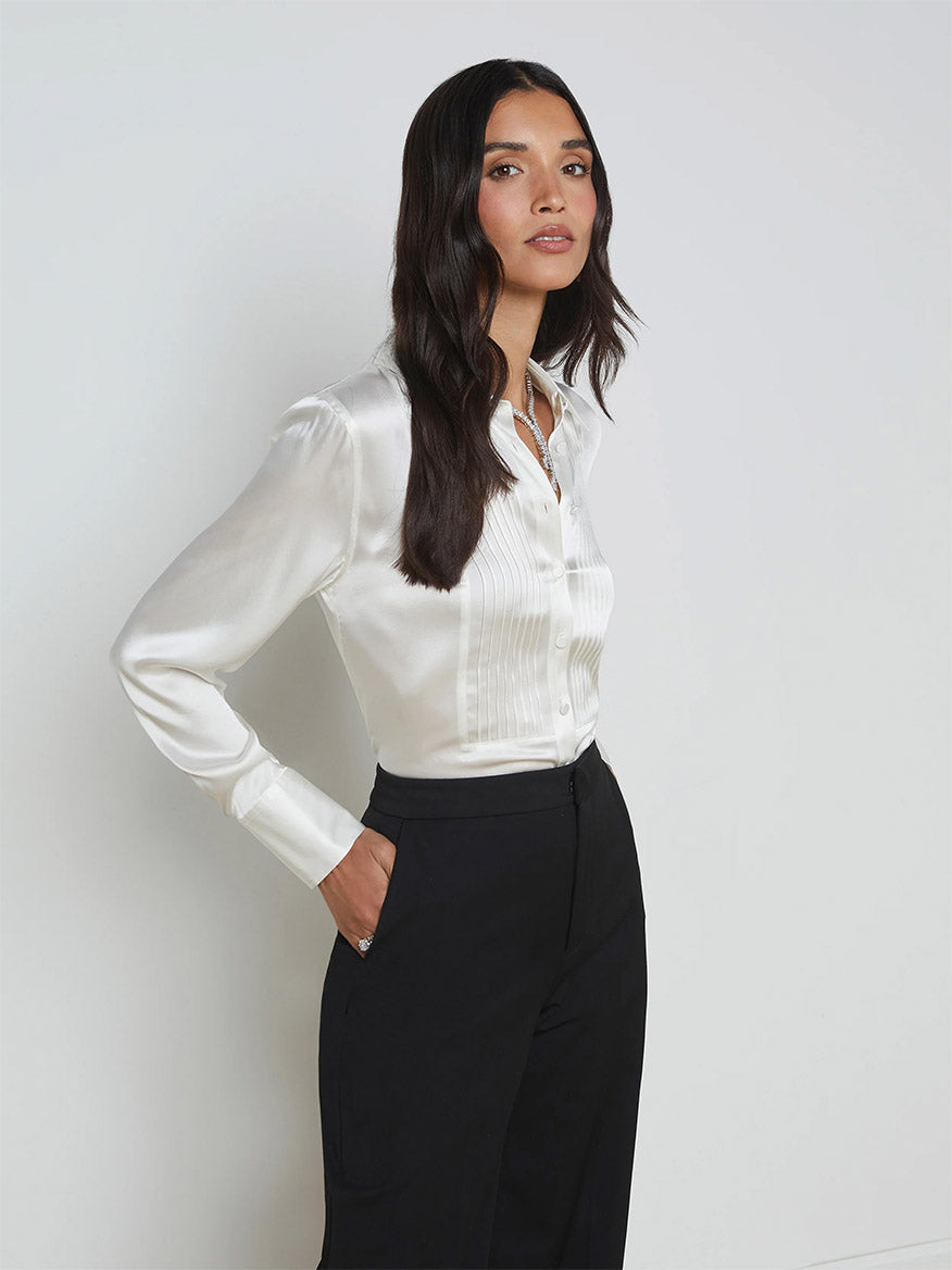 A person wearing the L'Agence Divya Silk Shirt in White and black pants stands against a plain background, looking slightly to the side.