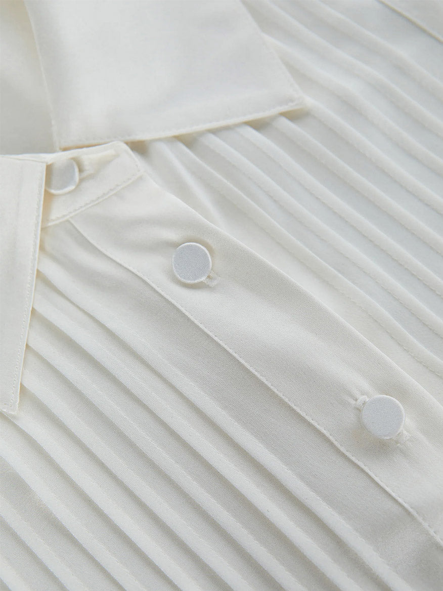 A close-up of the L'Agence Divya Silk Shirt in white showcases its pleated fabric and collar, adorned with satin-covered button closures that add an elegant touch.