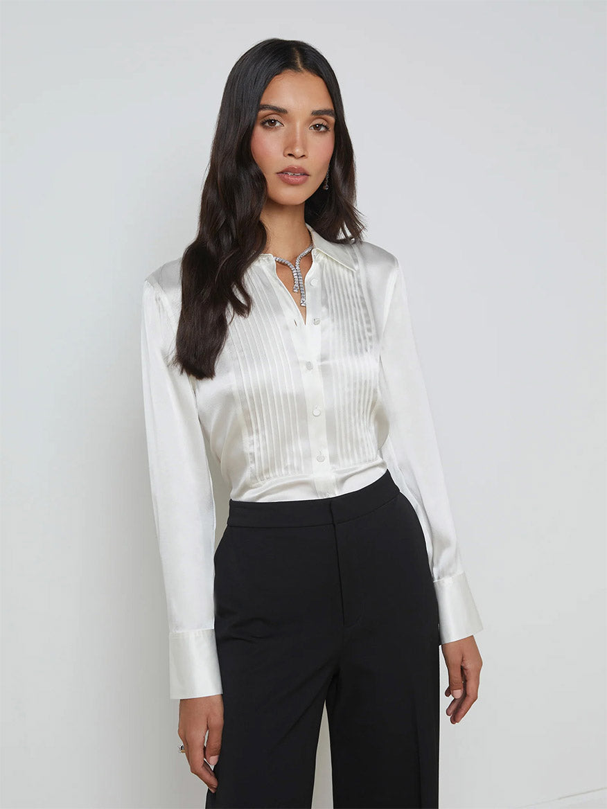 An individual dressed in the L'Agence Divya Silk Shirt in white, paired with black pants, standing against a plain background.