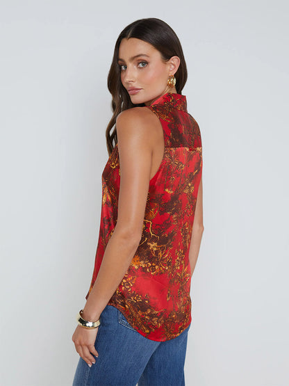 Woman with long dark hair wearing a vibrant L'Agence Emmy Sleeveless Blouse in High Risk Red Multi Jungle Toile and blue jeans, looks over her shoulder.