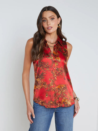 A person with long, dark hair stands against a plain background, wearing the L'Agence Emmy Sleeveless Blouse in High Risk Red Multi Jungle Toile and blue jeans.