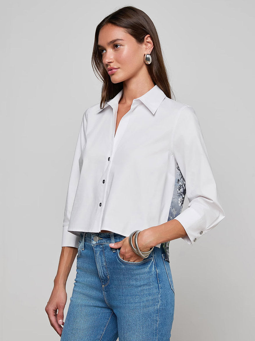 A woman wears the L'Agence Fawn Panther Print Shirt in Ivory Multi Floral Panther Scarf with blue jeans, standing against a plain gray background.